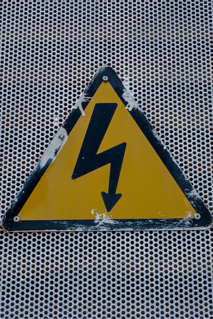 High voltage warning sign on a metal grid background, indicating electrical hazard.