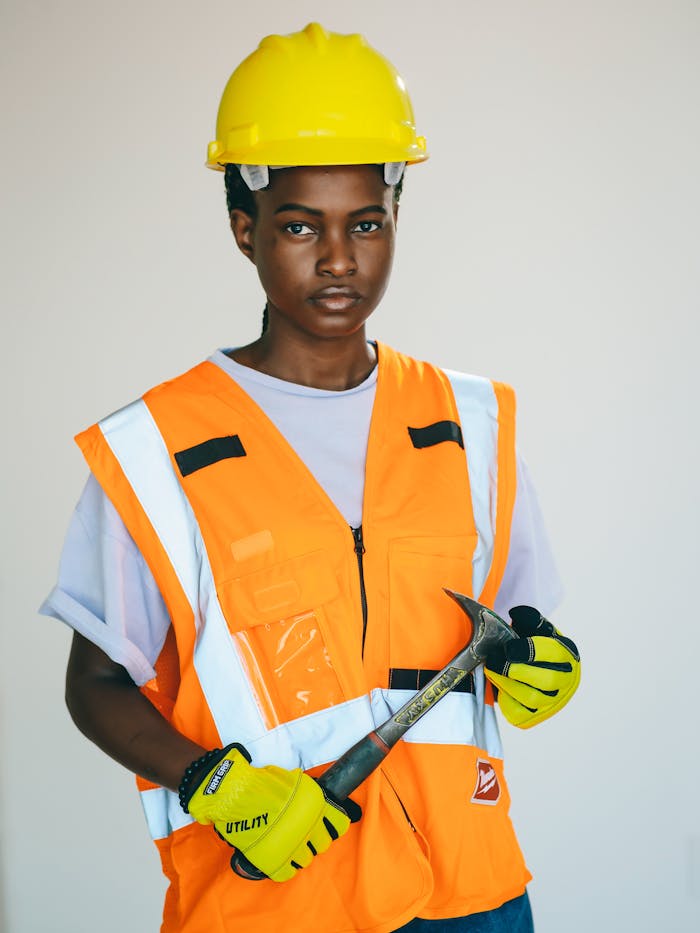 African American woman in safety gear holding a hammer confidently in a studio setting.