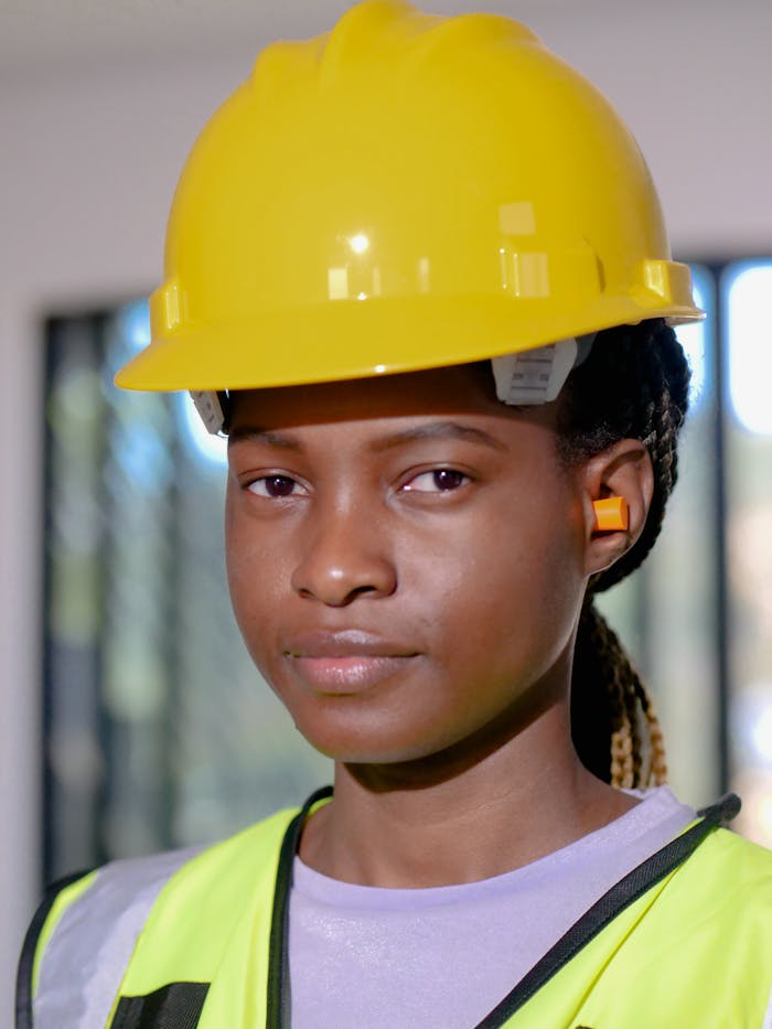 Portrait of a woman in construction gear with hardhat and ear protection indoors.